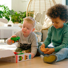 Two young children playing on the floor together with the green Smartmax My First Farm Tractor set, assembling the magnetic pieces near the open product box.