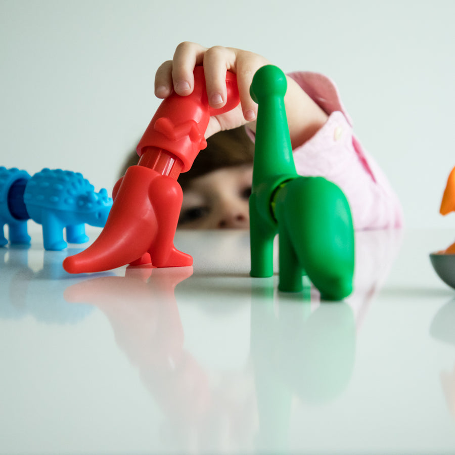 Child playing with colorful dinosaur toys on a reflective surface.
