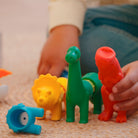 Colorful plastic animal toys on a carpeted floor with a child's hand holding a red toy.