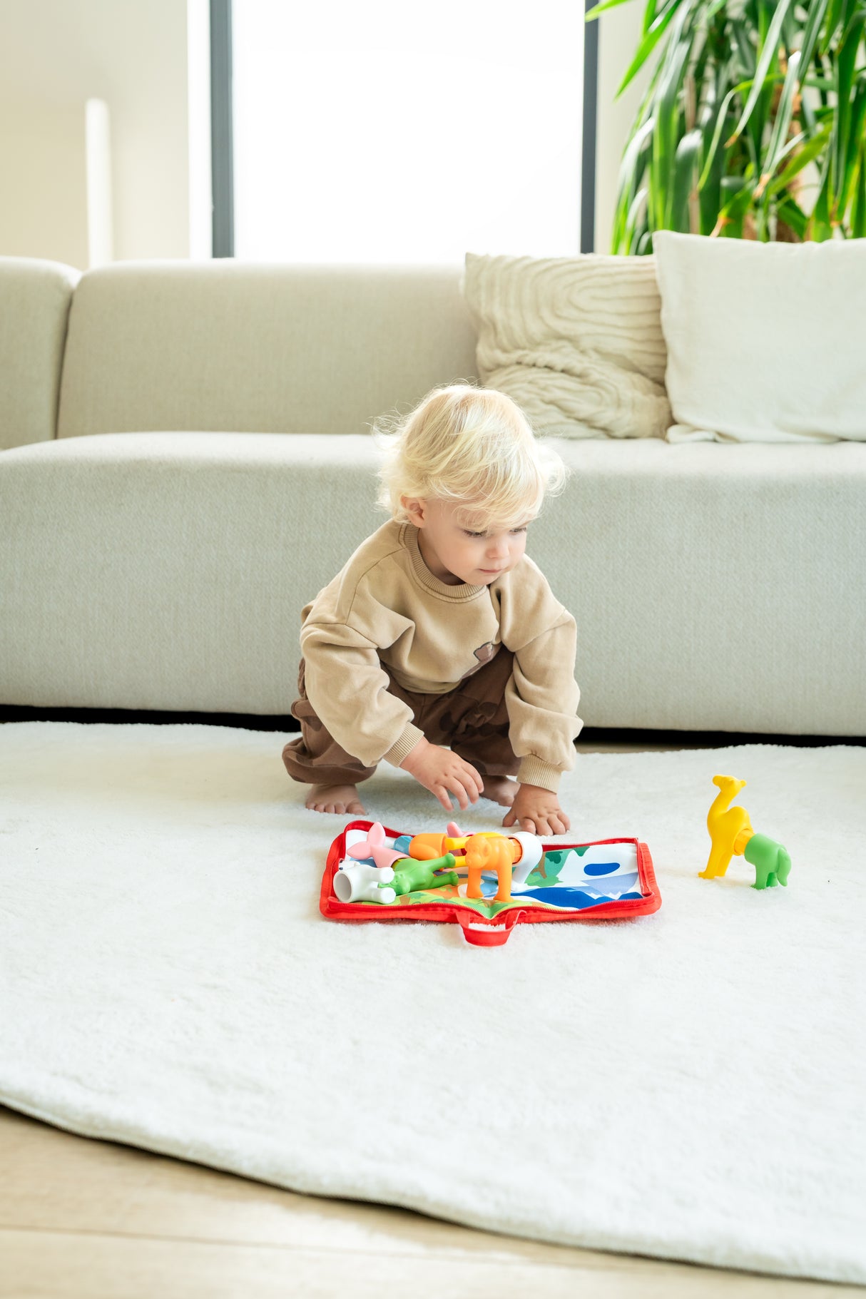 Child playing with toys on a white blanket in a living room.