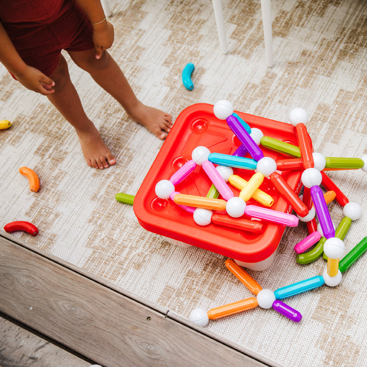 Colorful toy building blocks on a red tray with a child's legs in the background.