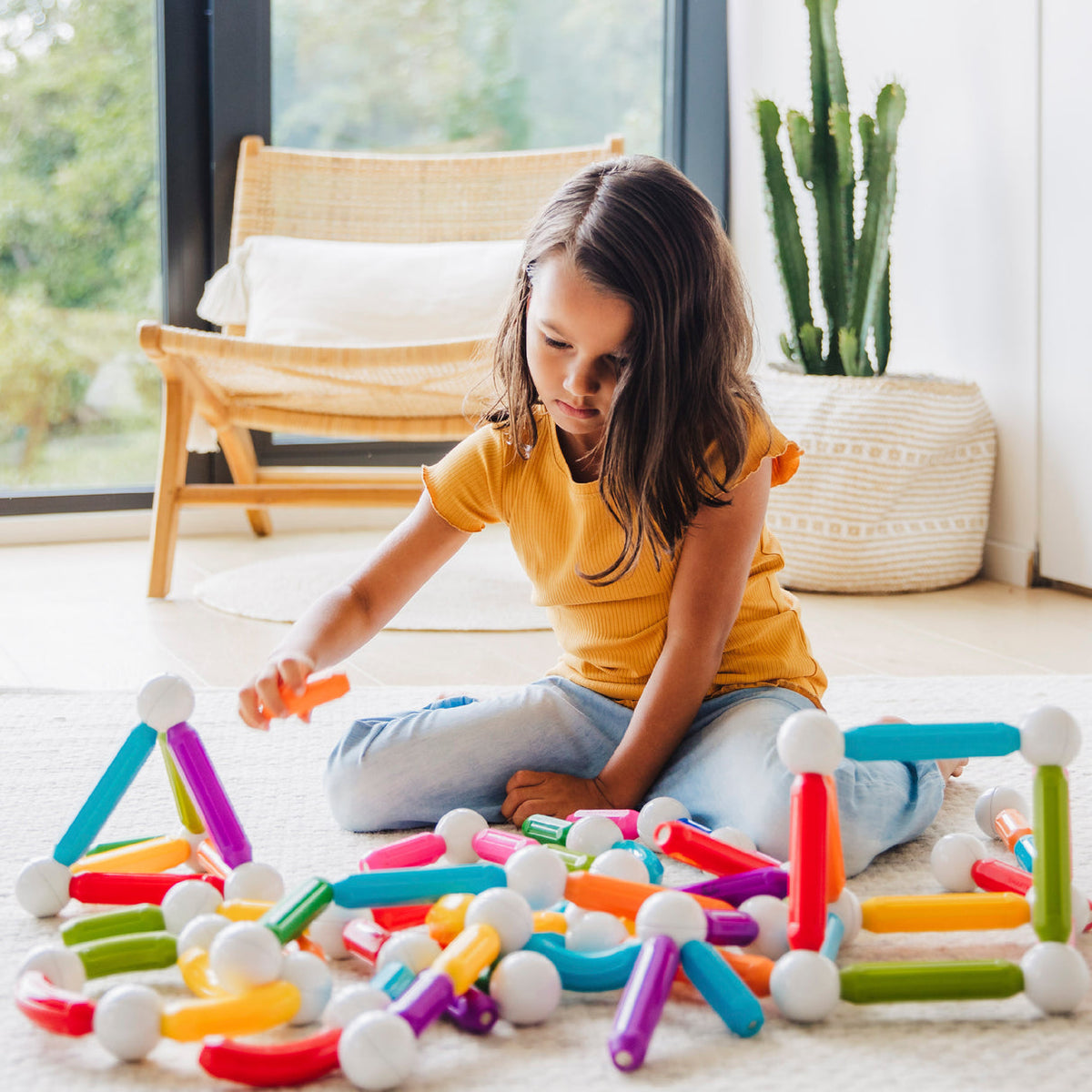 Child playing with colorful building toys on a light-colored floor.