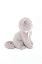 A soft grey plush kitten toy viewed in profile, showing its seated posture, curved tail, and a white satin ribbon bow tied around its neck.