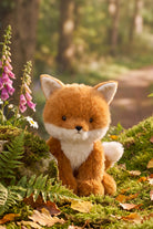 A plush toy fox sitting on a rustic wooden stump surrounded by blooming spring flowers, greenery, and autumn leaves.