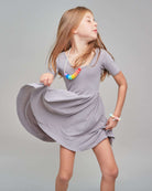 Young girl in a gray dress with a colorful necklace against a plain background