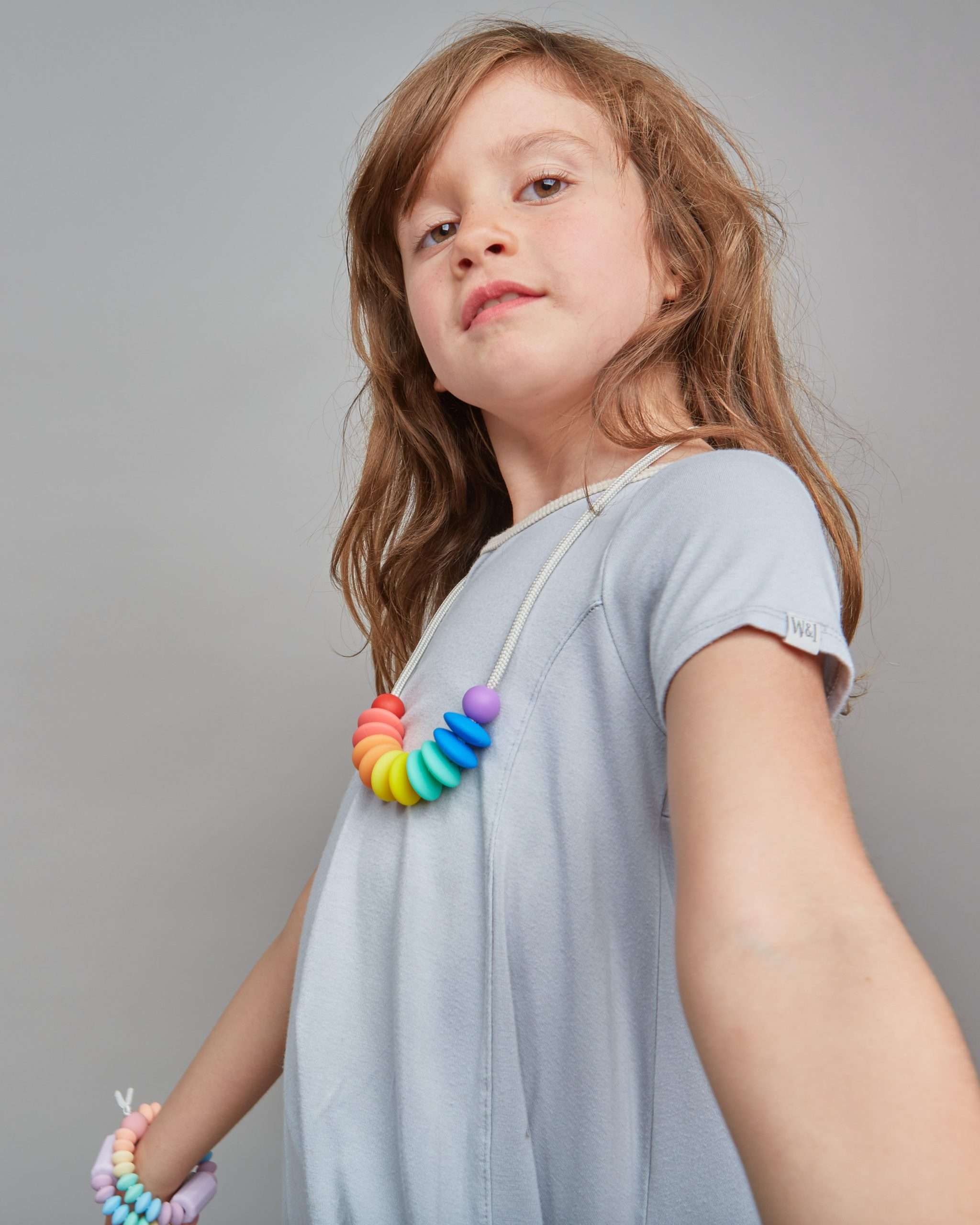 Young girl wearing a colorful necklace against a plain background
