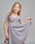 Young girl wearing a gray dress with a colorful necklace against a gray background