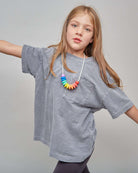 Young girl wearing a gray oversized t-shirt and colorful necklace on a plain background
