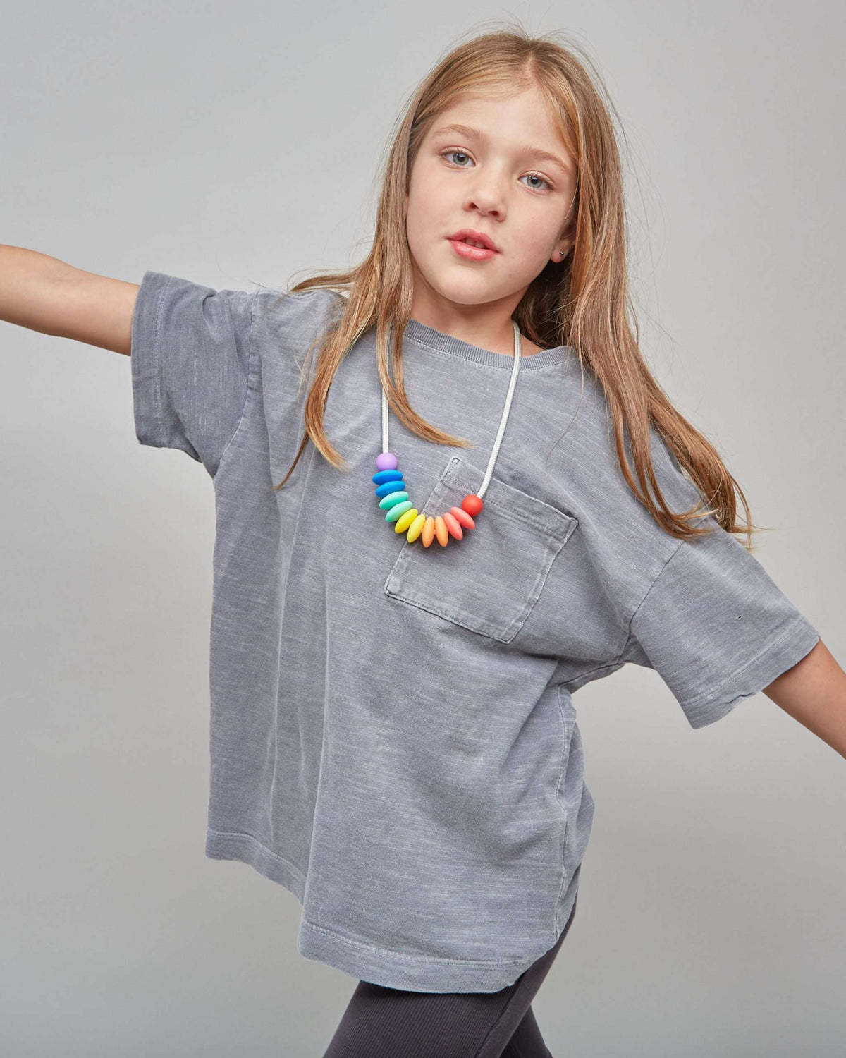Young girl wearing a gray oversized t-shirt and colorful necklace on a plain background