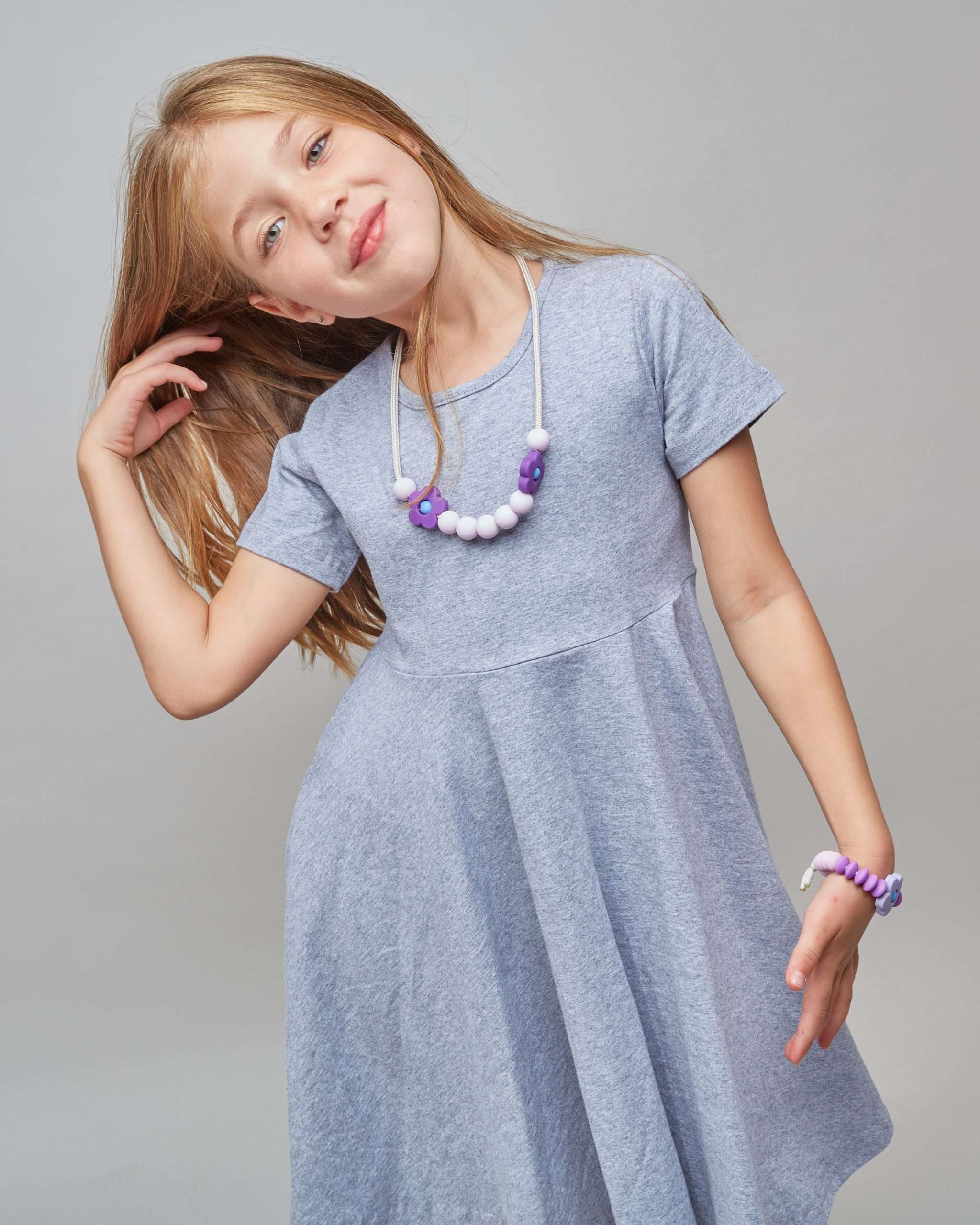 Young girl wearing a gray dress with a necklace on a plain background