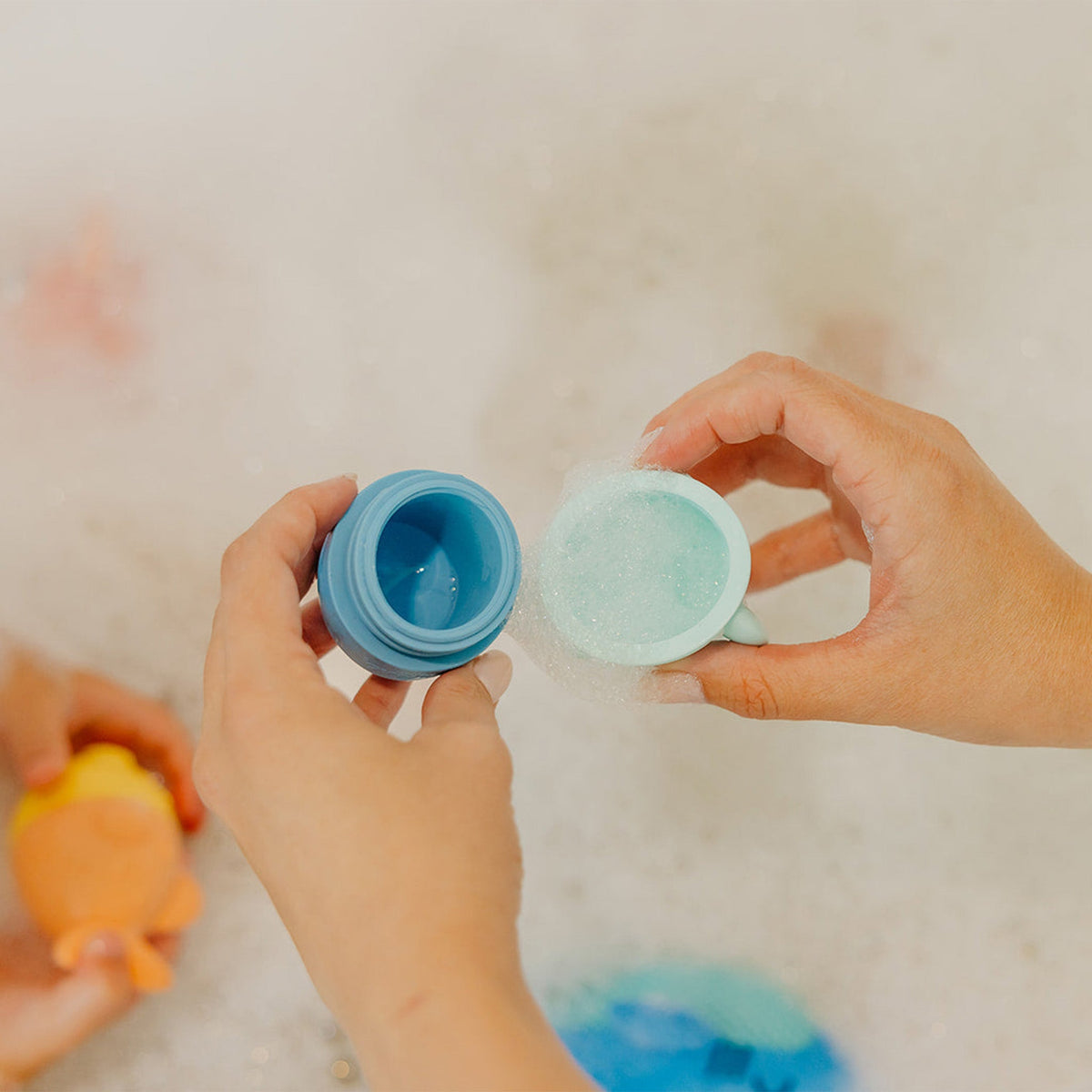 Two hands holding blue and green containers with a neutral background