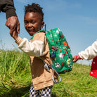 Child with a colorful backpack being held by an adult in a grassy field