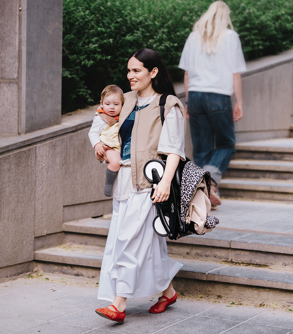Woman holding a baby and carrying bags on a city street