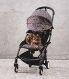 Cat lying inside a baby stroller with leopard print cover on a concrete floor.