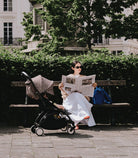 Woman reading a newspaper on a bench with a stroller next to her