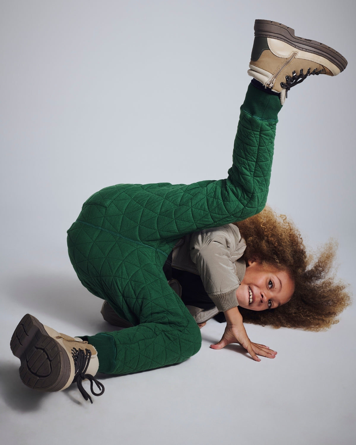 Person wearing green quilted pants and brown boots on a plain background