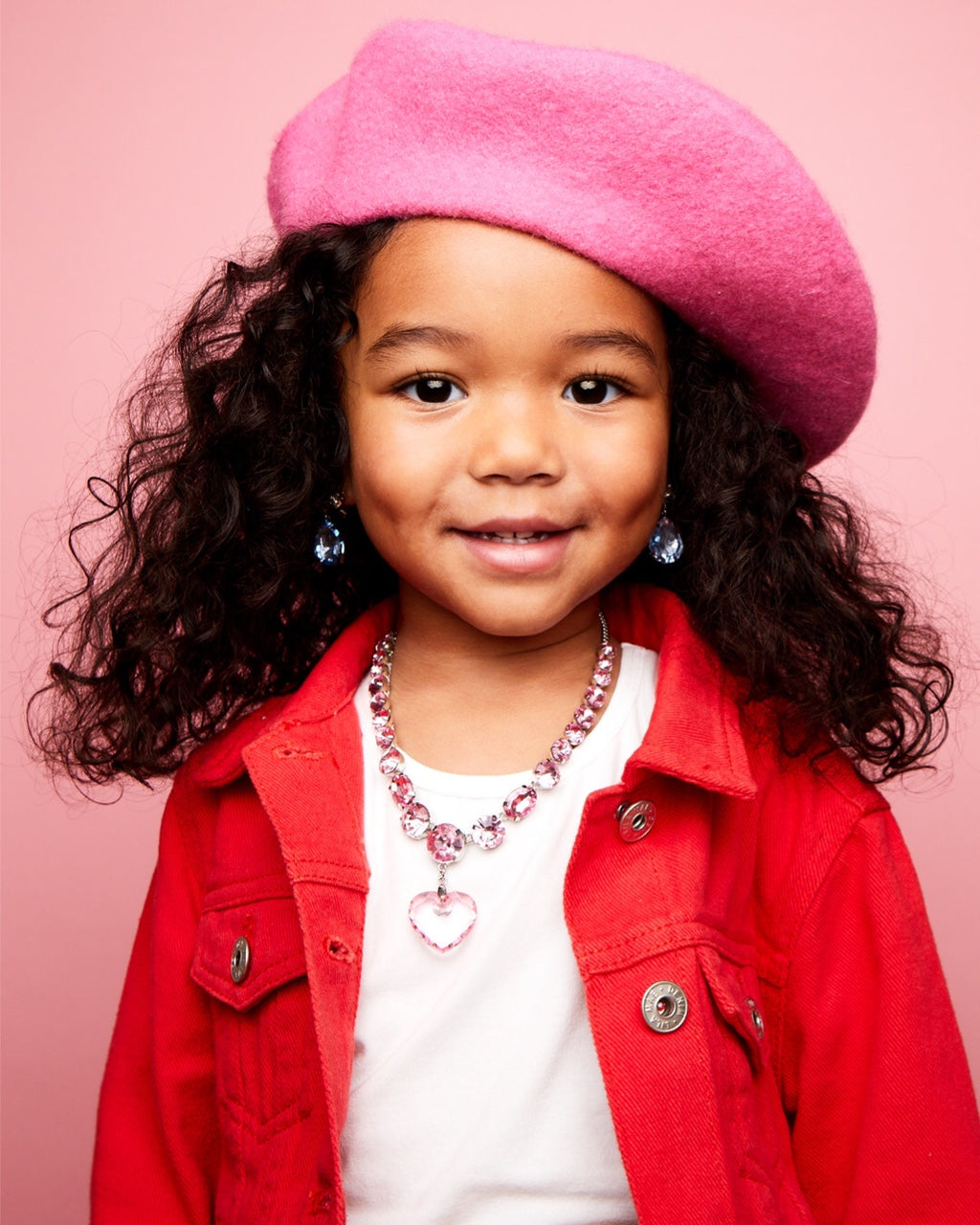 Child wearing a pink beret and red jacket against a pink background