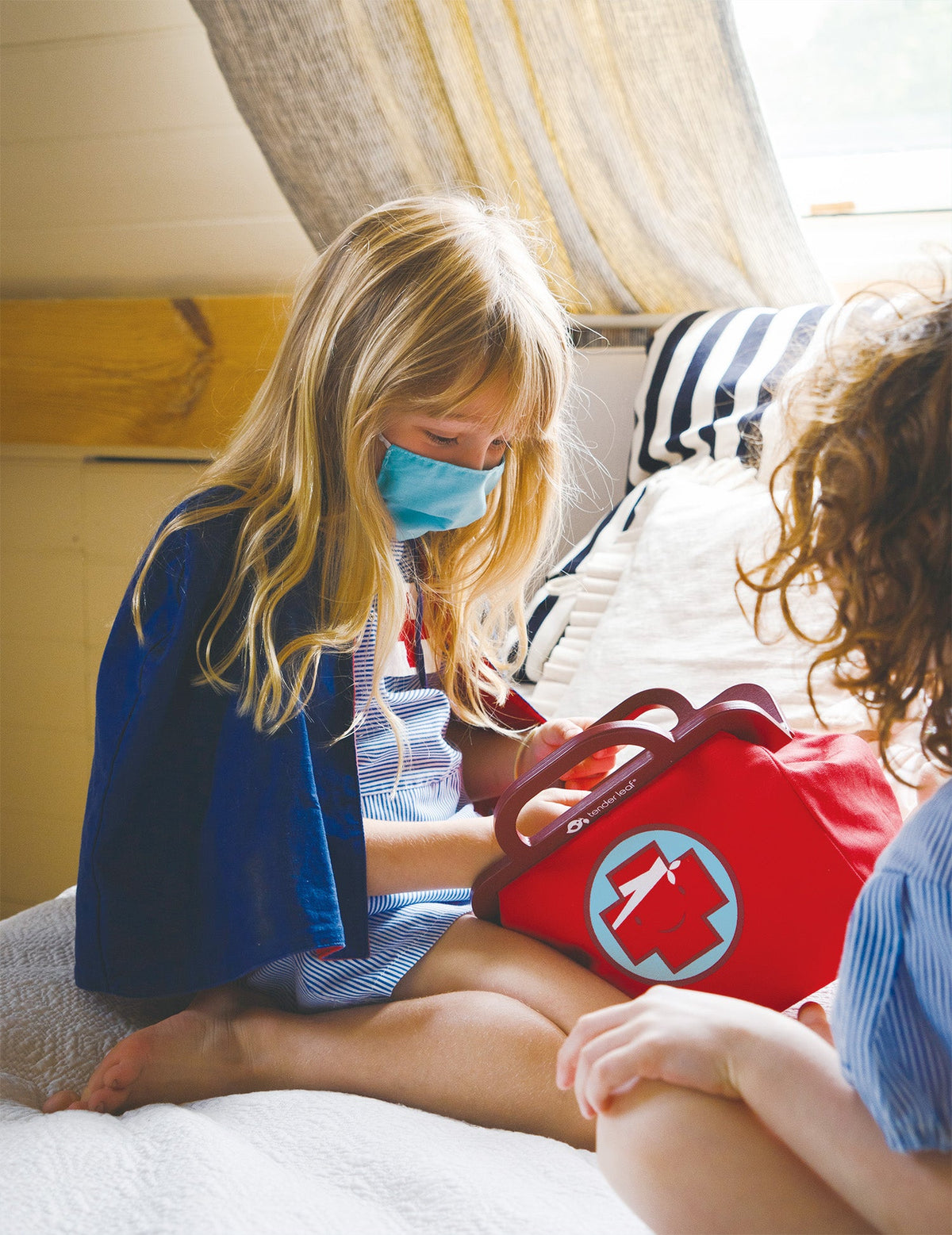 Two children with a first aid kit on a bed