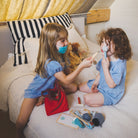 Two children playing with toy medical equipment on a bed.