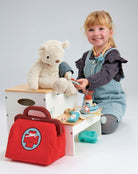 Child playing with toys including a teddy bear, toy bag, and wooden blocks on a white background