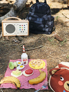 Picnic setup with food, drinks, and a radio on a checkered blanket outdoors.