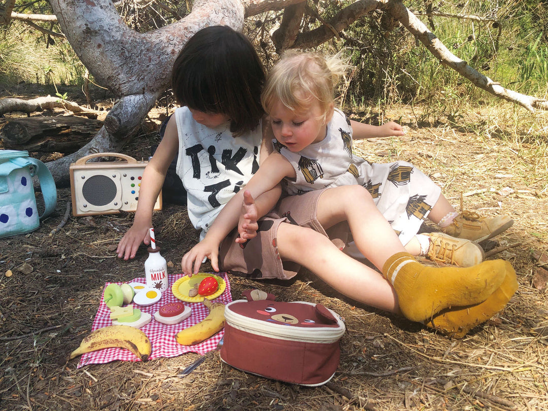 Two children sitting on the ground with a picnic setup in a natural setting.