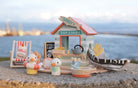 Toy set with a beach hut, boat, and seagulls on a stone surface with water in the background