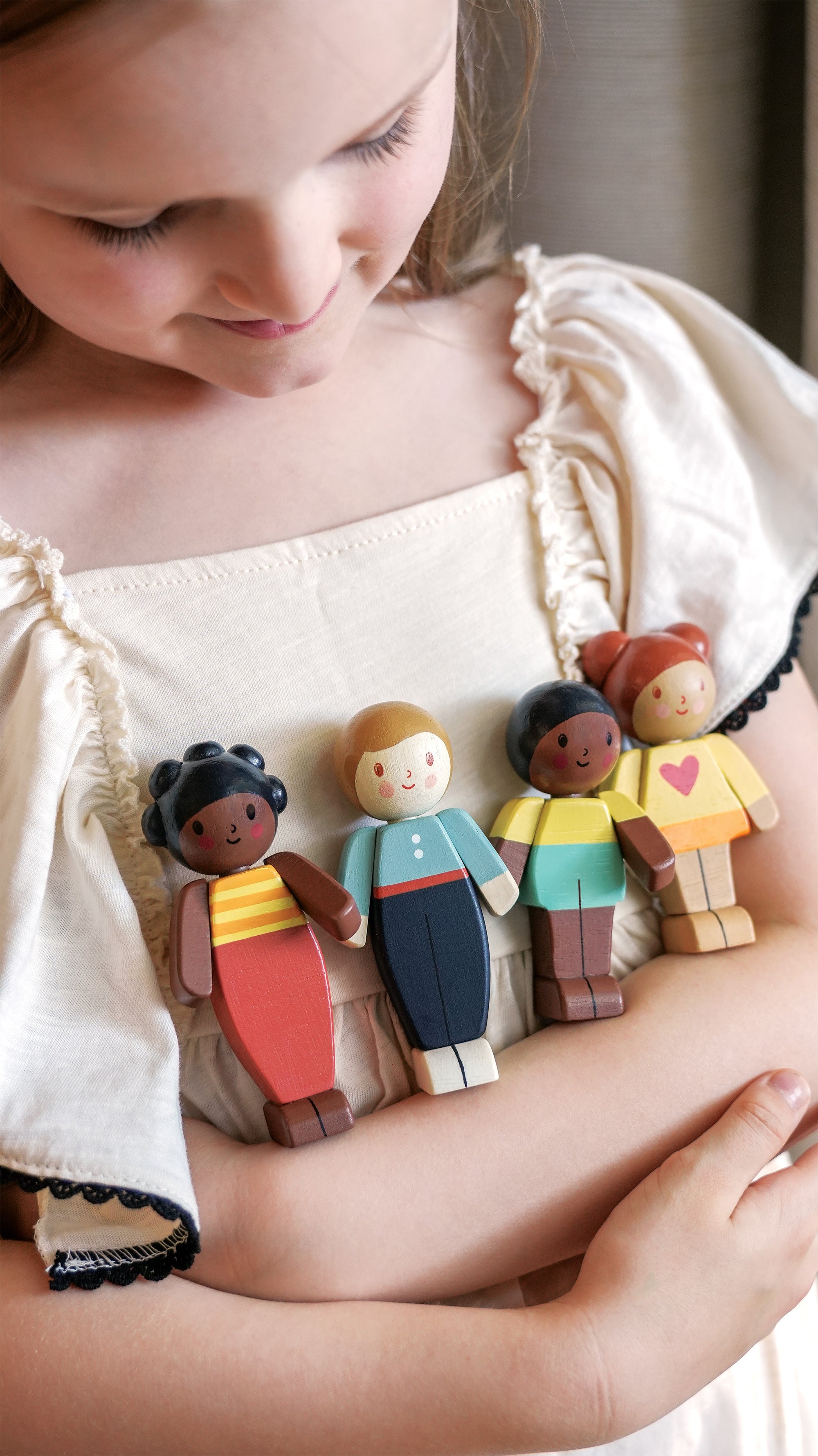 Child holding a set of diverse wooden toy figures