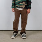 Person wearing a camouflage jacket, brown pants, and black sneakers on a plain background