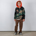 Child wearing a camouflage jacket with an orange hood against a white background