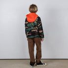Child wearing a camouflage hoodie with an orange hood against a plain background