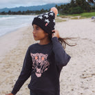 Child on a beach wearing a star-patterned beanie and sweatshirt with a tiger design.