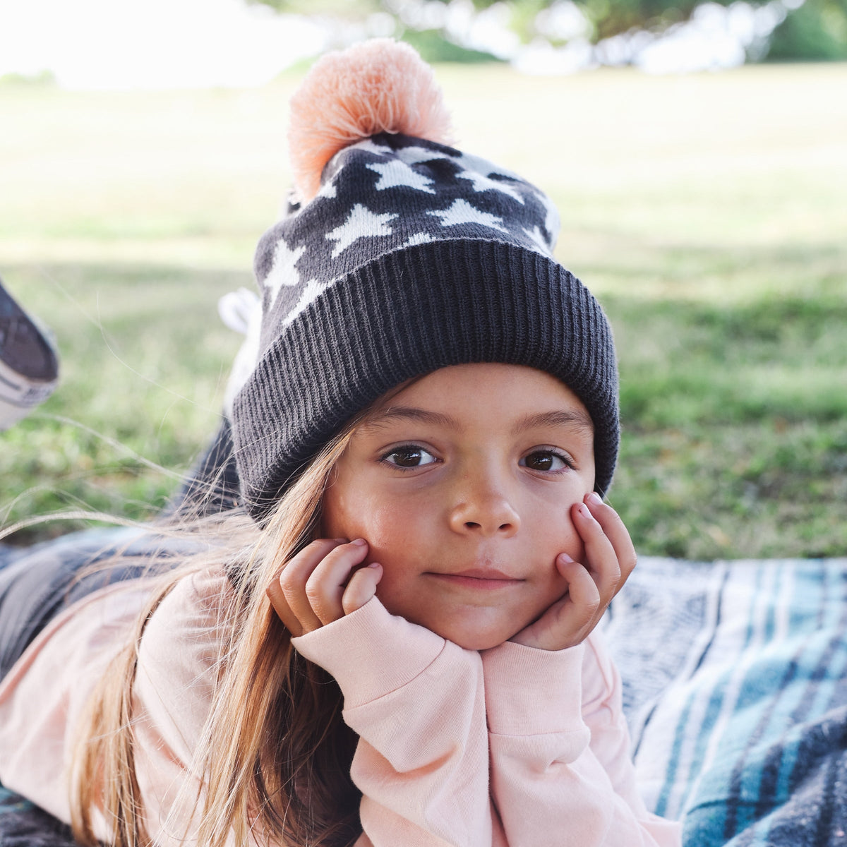 Child wearing a star-patterned beanie with a pom-pom outdoors