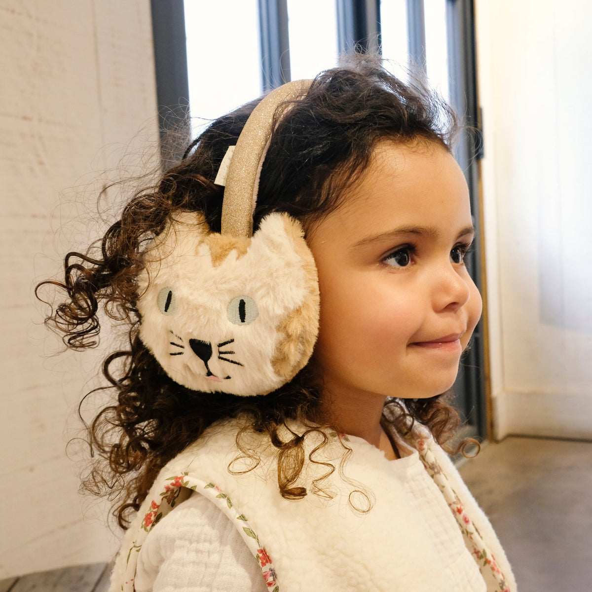 Child wearing a fluffy animal-themed earmuff indoors