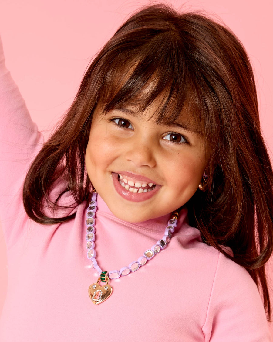 Young girl wearing a pink shirt and colorful necklace against a pink background