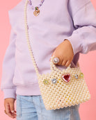 Person holding a pearl-handled handbag with decorative elements against a pink background