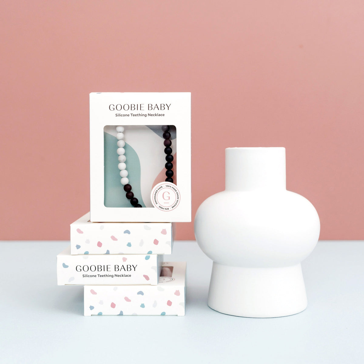 GOOBIE BABY silicone teething necklace packaging with a white vase on a pink background