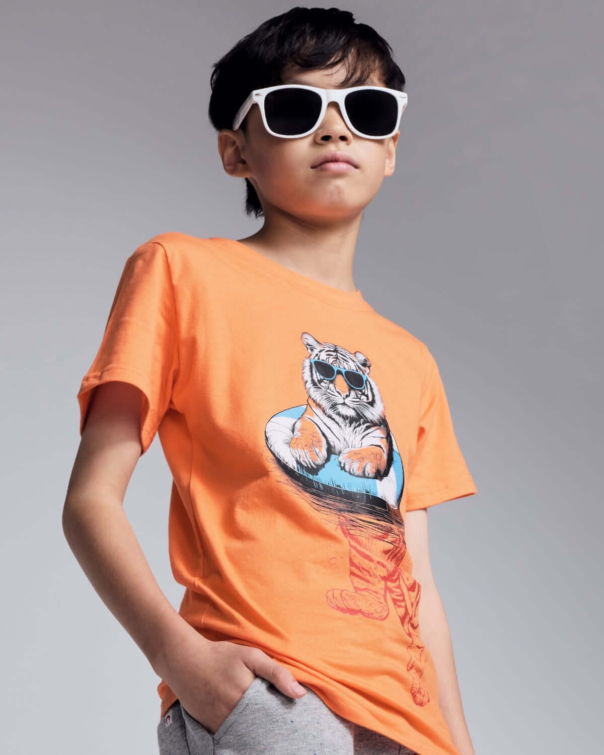 Child wearing an orange t-shirt with a tiger graphic and sunglasses on a gray background