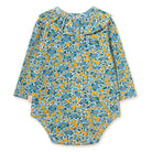A long-sleeve baby bodysuit with a dense floral print in blue, yellow, and green, featuring a ruffled neckline and snap closures at the crotch.