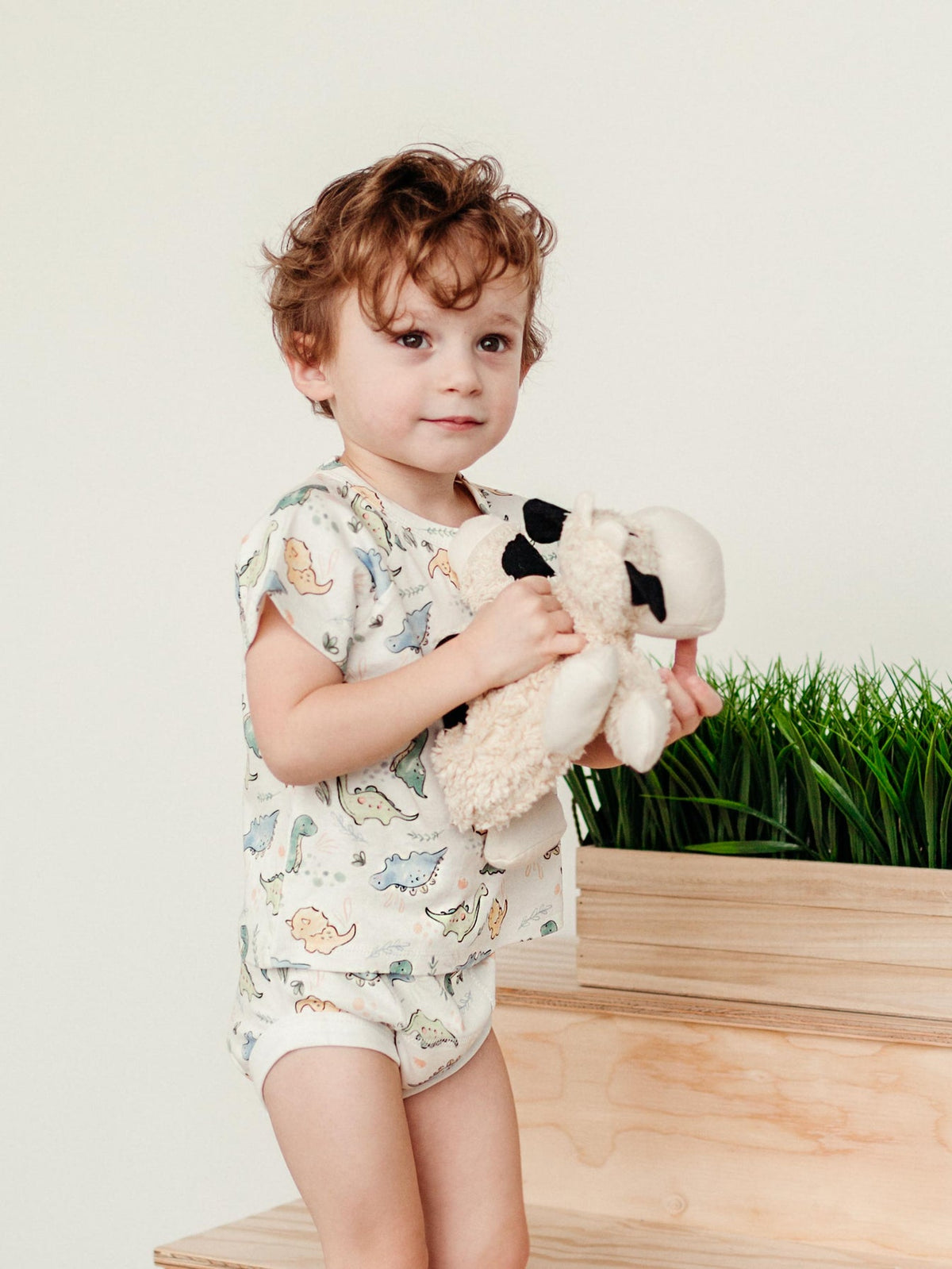 Child holding a plush toy outdoors with a wooden bench and grass in the background