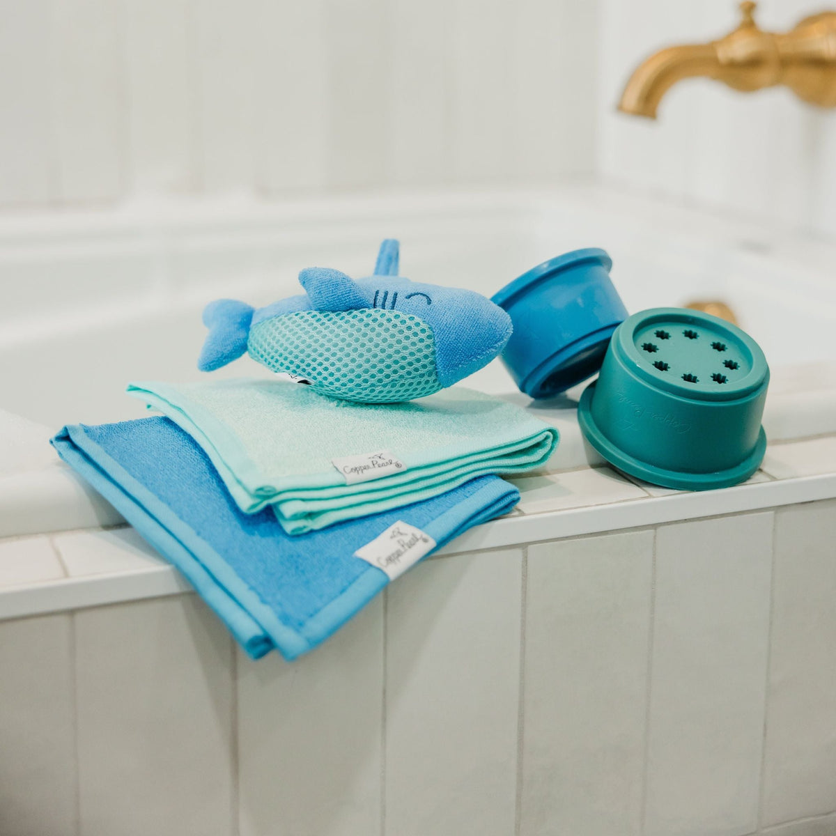 Bath toys including a shark-shaped item, a blue sponge, and a green scrubber on a bathtub ledge.