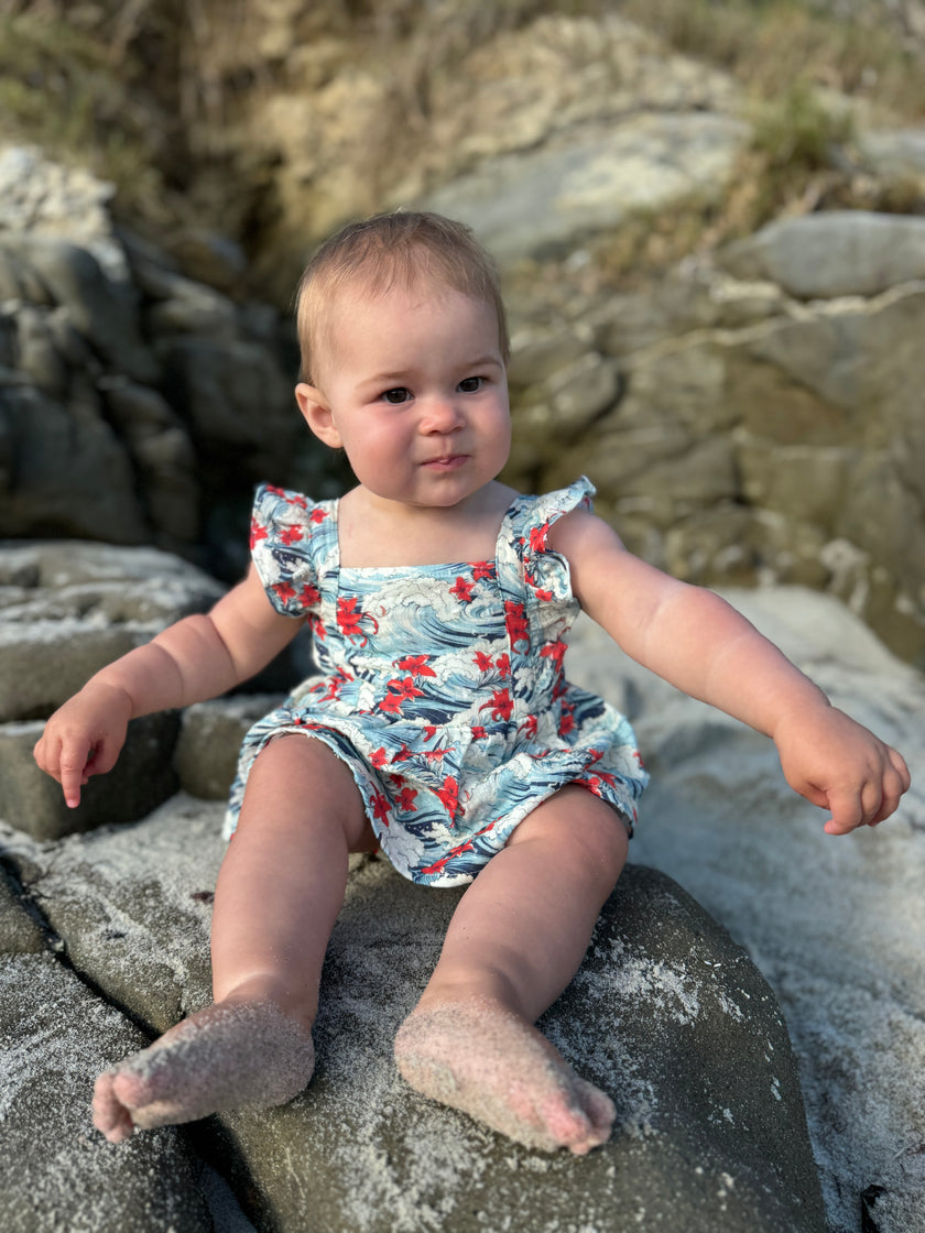 Baby sitting on rocks by the sea wearing a colorful swimsuit.