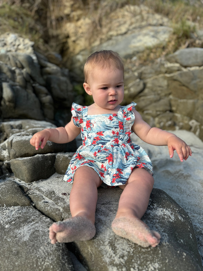 Baby in a floral romper sitting on rocks at the beach
