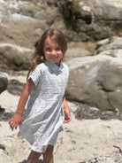 Young girl in a blue dress standing on a rocky beach