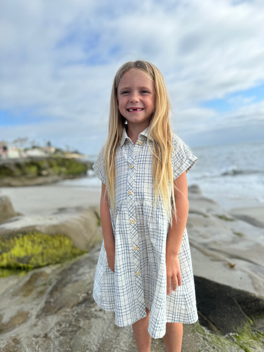 Young girl in a checkered dress standing on a beach with ocean and sky in the background