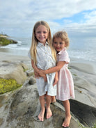 Two young girls standing on a rocky beach with ocean and sky in the background