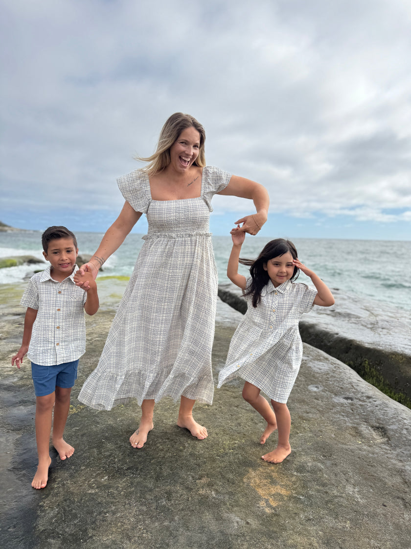 Woman and two children in matching outfits standing on a stone ledge by the ocean.