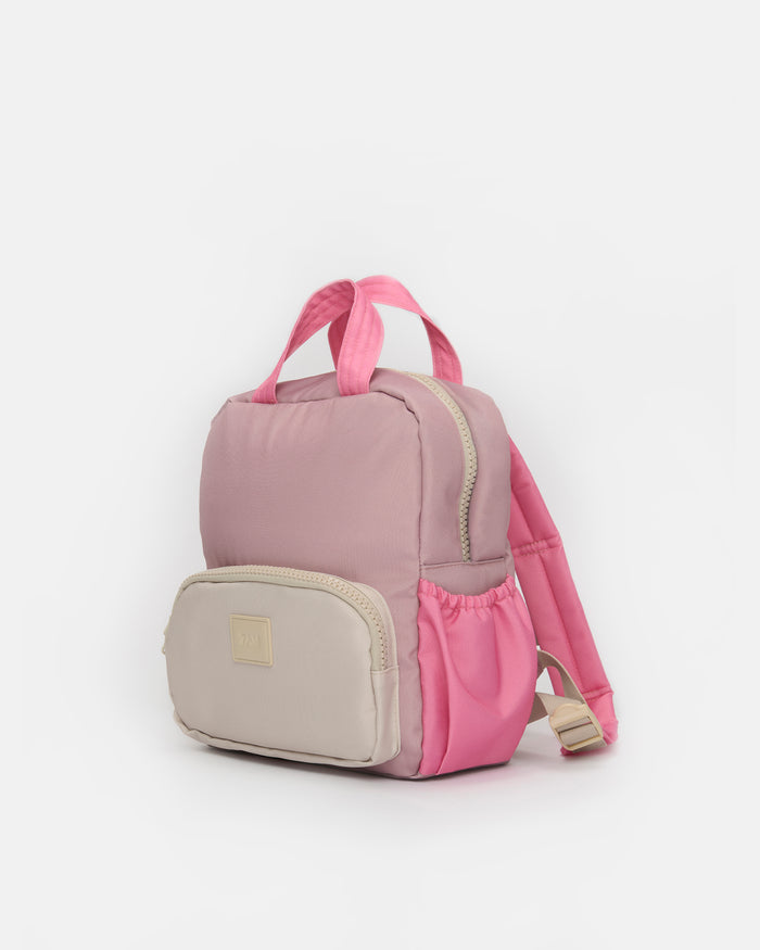 A small pink and beige backpack with dual top handles, a front zippered pocket, and a side mesh pocket, shown on a plain light gray background.