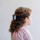 Child with curly hair wearing a blue hair clip against a plain background