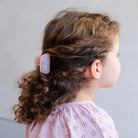 Child with braided hair wearing a pink shirt against a plain background